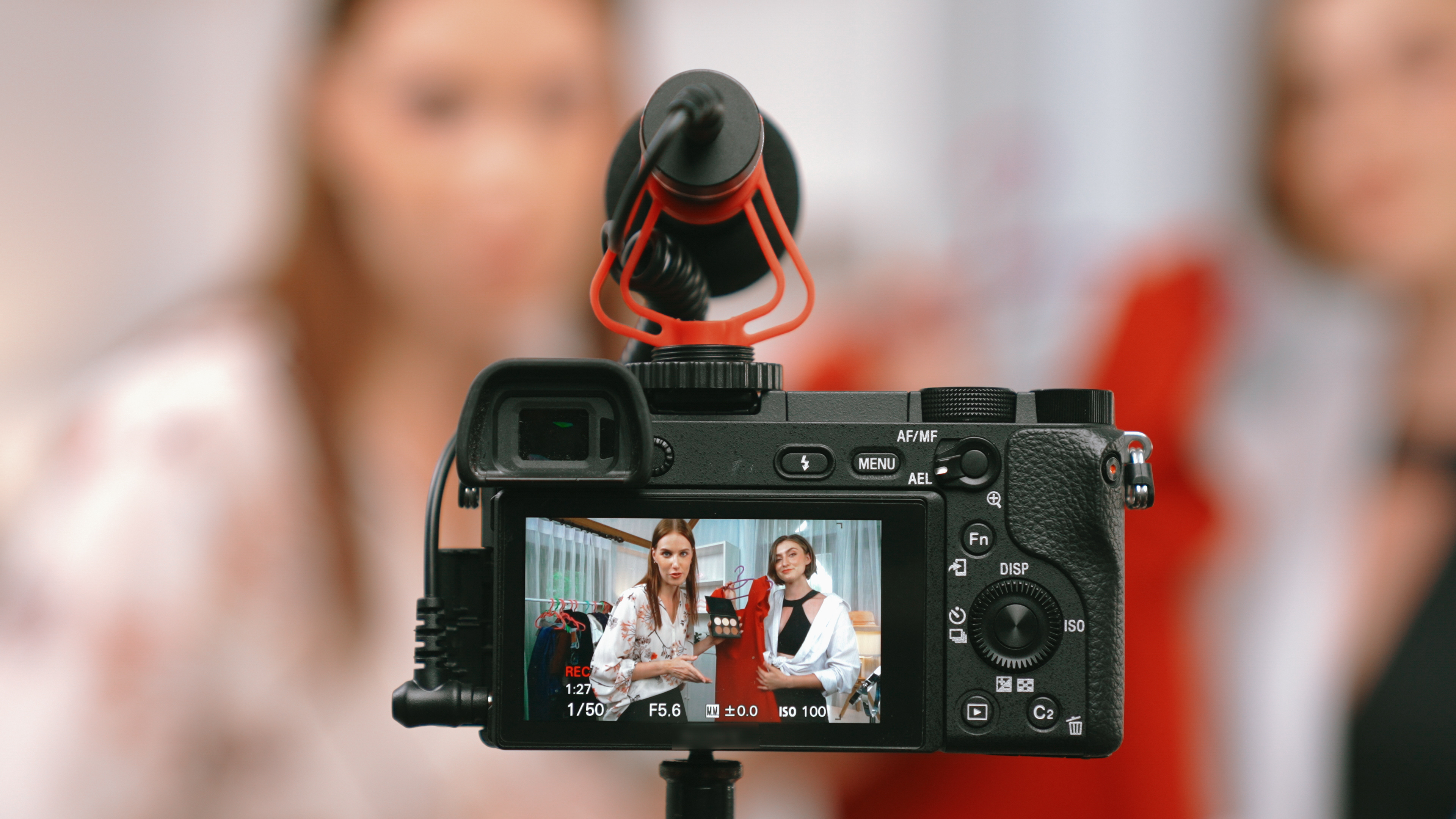 A content creator filming a video, reviewing footage on a camera screen with a directional microphone attached