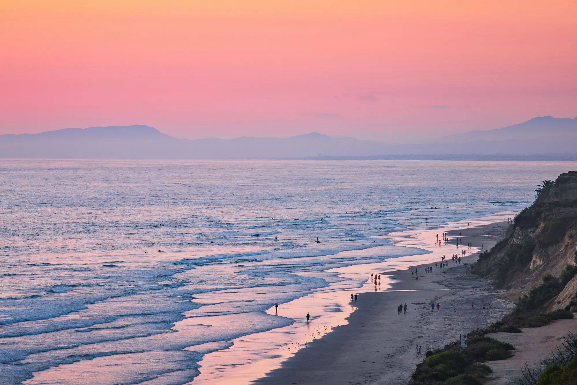 Del Mar, California coastline at sunset with beachgoers along the shore and mountains in the distance